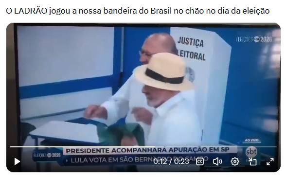 A imagem exibe uma captura de tela de um reprodutor de vídeo encabeçada pelo texto 'O LADRÃO jogou a nossa bandeira do Brasil no chão no dia da eleição'. A cena reproduzida mostra dois homens de pele clara em um ambiente com móveis e paredes azuis e brancas. Em primeiro plano, um homem com barba grisalha, vestindo camisa branca e um chapéu claro com faixa escura, segura um tecido verde na altura da cintura. Logo atrás, um homem calvo, usando óculos e também de camisa branca, estende o braço direito em direção ao objeto verde. Ao fundo, observa-se uma estrutura branca de votação com a inscrição 'JUSTIÇA LEITORAL'. Na parte inferior do quadro, controles típicos de reprodução de vídeo estão sobrepostos a gráficos de transmissão televisiva, que incluem o logotipo 'sbt', a indicação 'AO VIVO' e as tarjas informativas 'PRESIDENTE ACOMPANHARÁ APURAÇÃO EM SP' e 'LULA VOTA EM SÃO BERNARDO DO CAMPO'.