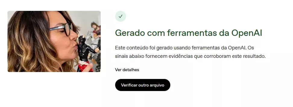 A imagem apresenta uma composição dividida em duas áreas. À esquerda, exibe-se a fotografia de perfil de uma mulher de pele clara e cabelos longos e ondulados, com raiz castanha e pontas loiras. Ela usa óculos de grau com armação escura, está com os olhos fechados e com os lábios encostados em uma pequena estátua preta com chifres brancos e vestes vermelhas. À direita, sobre um fundo branco, há uma interface que exibe um ícone circular verde claro com um sinal de visto no centro e o título 'Gerado com ferramentas da OpenAI'. Abaixo desse título, encontra-se o texto explicativo 'Este conteúdo foi gerado usando ferramentas da OpenAI. Os sinais abaixo fornecem evidências que corroboram este resultado.', seguido pelo texto 'Ver detalhes' e um botão de fundo preto com a inscrição em branco 'Verificar outro arquivo'.