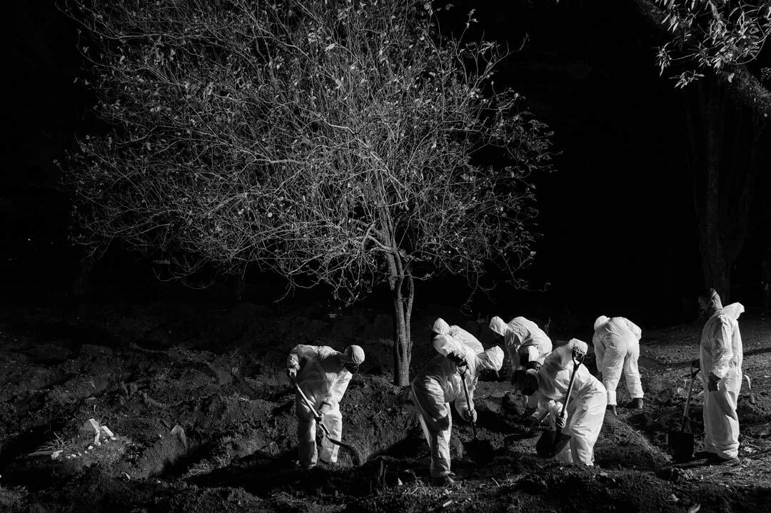 Com roupas protetoras, trabalhadores fazem um sepultamento à noite de uma vítima da Covid-19.